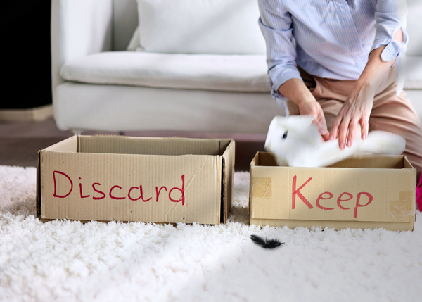 Person sorting belongings into boxes labeled "Discard" and "Keep" on a white rug, symbolizing emotional decluttering personal growth.